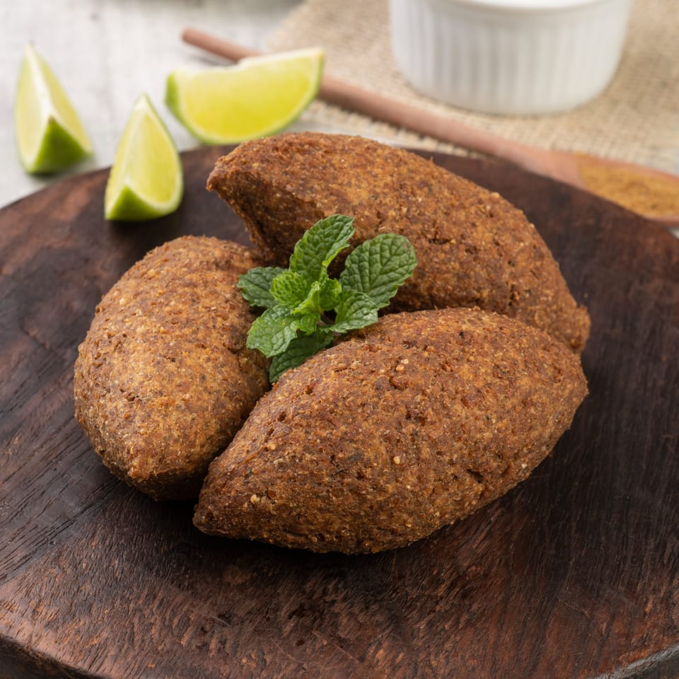 Three fried kibbeh with mint and lime wedges on a dark wooden board.