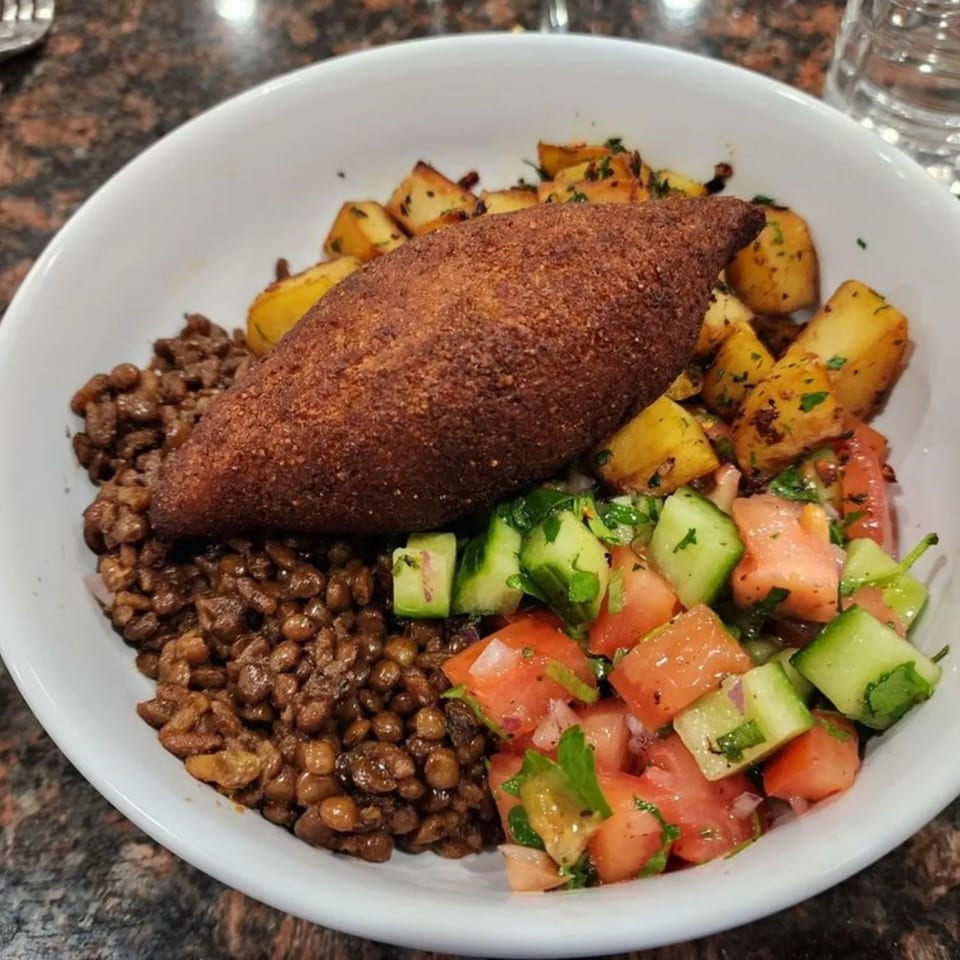 A middle-eastern dish with a fried kibbeh, lentils, roasted potatoes, and a cucumber tomato salad.