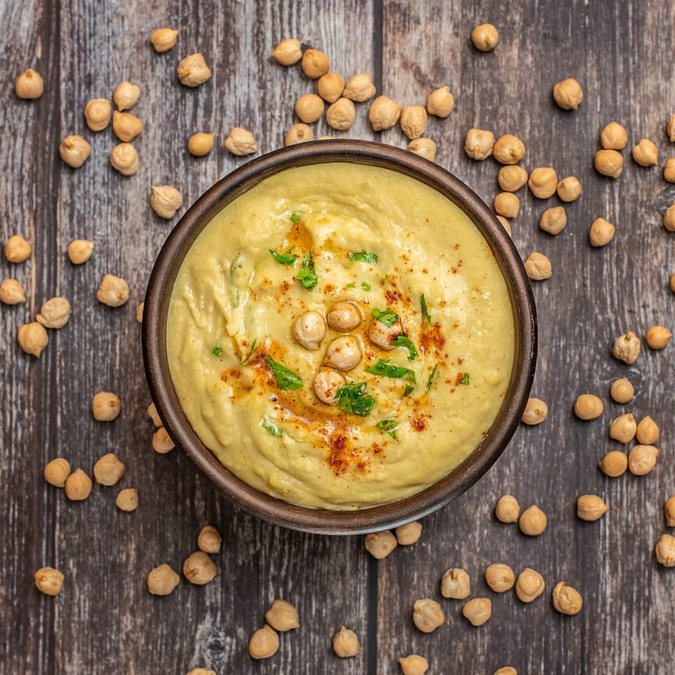 Casba Food and Pastries' hummus, garnished with chickpeas, paprika, and parsley, on a wooden table.